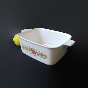 May include: White rectangular baking dish with a floral design featuring lemons, tomatoes, and herbs. The dish has two handles and says "L'Echalote" on the bottom.
