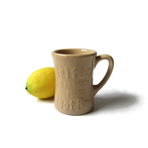 May include: A tan ceramic mug with a handle. The mug has the words "Solves Every Problem" embossed on the side. A yellow lemon is next to the mug.