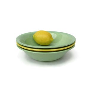 May include: Three green bowls stacked on top of each other, with a yellow lemon on top of the bowls.