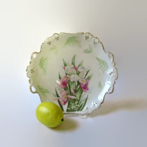 May include: A white porcelain serving dish with a scalloped edge and gold trim. The dish features a floral design of pink and white irises with green leaves.