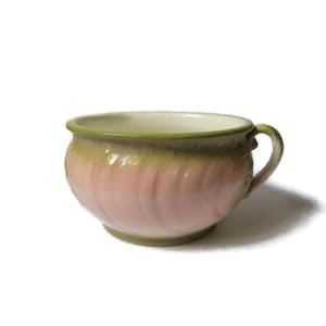 May include: A pink and green ceramic planter with a rounded shape and a single handle. The planter has a textured, rippled design.