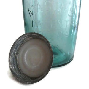 May include: A vintage green glass Mason jar with a metal lid. The jar has the text "MASON'S PATENT" embossed on the side.