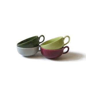 May include: Four ceramic teacups stacked on top of each other. The top cup is green, the second is light green, the third is gray, and the bottom cup is burgundy.