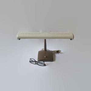 May include: A white vintage desk lamp with a brown base and a patterned shade. The lamp is turned on and the light is shining.