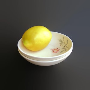 May include: A yellow lemon sits in a white bowl with a floral design. The bowl is stacked on top of another white bowl.