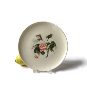 May include: A white ceramic dinner plate with a pink rose and green leaves design.