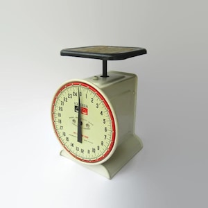 May include: Vintage cream-colored Hanson kitchen scale with a black platform and a red-trimmed dial. The dial displays numbers from 0 to 24 pounds. The scale has a classic design, perfect for measuring ingredients.