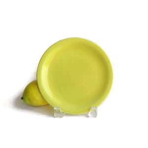 May include: A bright yellow ceramic plate with a slightly raised rim. The plate is on a white background.