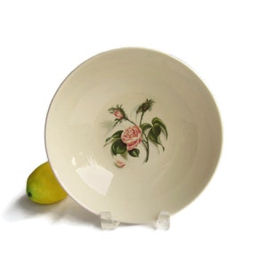 May include: A white ceramic bowl with a pink rose and green leaves design. The bowl is empty and has a smooth, glossy finish.