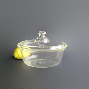 May include: A clear glass butter dish with a lid. The dish has a rounded shape and a smooth surface. The lid has a knob on top.