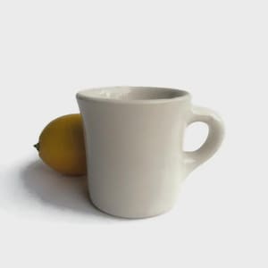 May include: A white ceramic mug with a rounded handle. The mug is a classic diner style.