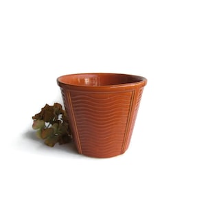 May include: A terracotta-colored ceramic planter with a wavy pattern. The planter is empty and has a smooth, glazed finish.