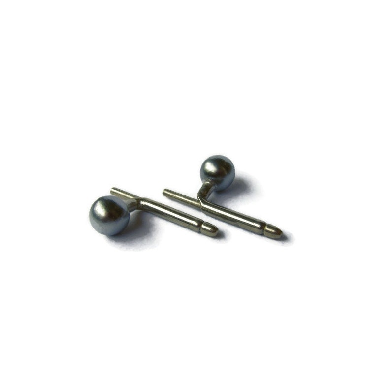 May include: A pair of silver cufflinks with a grey pearl on each end. The cufflinks are in the shape of a small, angled bar.