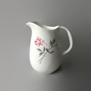 May include: A white ceramic mug with a black handle and the text "But First, Coffee" in a handwritten style. The mug is on a white surface. The mug is approximately 4 inches tall.