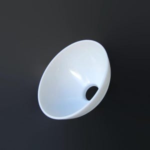 May include: A white, oval-shaped ceramic bowl with a circular hole at the bottom. The bowl has a smooth, glossy finish and is set against a dark background. The design is simple and modern.