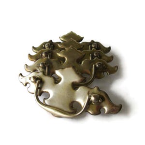May include: A collection of antique brass drawer pulls. Each pull features a stylized leaf design with a curved handle. The brass has a warm, aged patina, suggesting vintage craftsmanship. The pulls are arranged in a cluster.