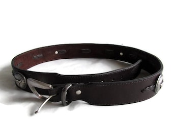 May include: A brown leather belt with a silver buckle and decorative metal accents. The belt has a braided design and is made of genuine leather.