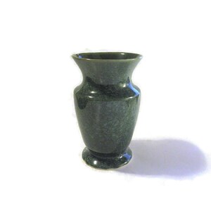 May include: A dark green ceramic vase with a speckled glaze. The vase has a rounded base and a narrow opening.