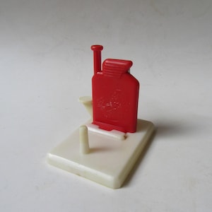 May include: A vintage red and off-white plastic cigarette lighter. The lighter is rectangular with a red top and a small, off-white base. The red portion has a design etched into it. The lighter is a collectible item.