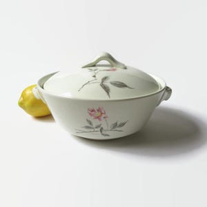 May include: White ceramic serving dish with a lid, featuring a floral design of pink roses and gray leaves. The dish has two handles on the sides.