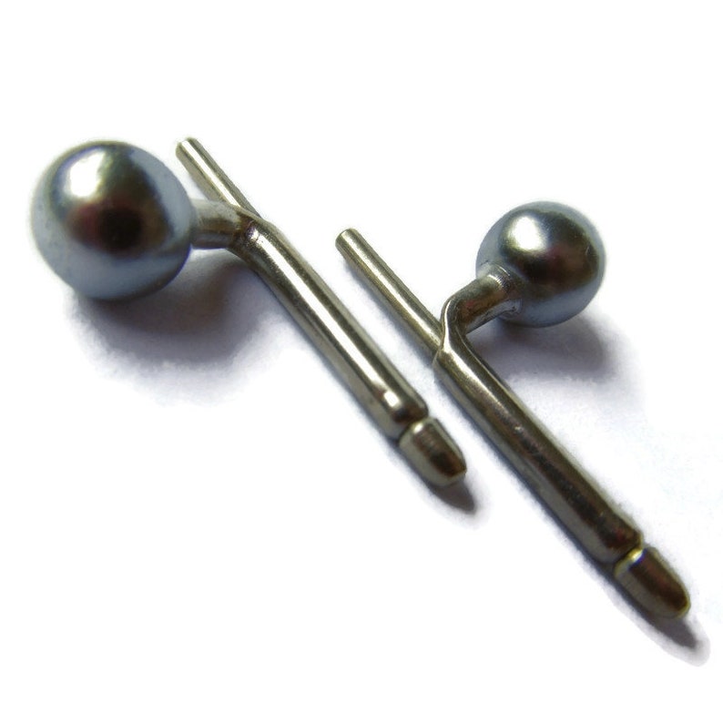 May include: A pair of silver cufflinks with a round, grey pearl on each end.