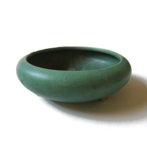 May include: A green ceramic planter with a rounded shape and three small feet. The planter is made of a matte finish ceramic.
