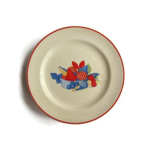 May include: A vintage white ceramic plate with a red rim and a colorful fruit design. The design features red, blue, and yellow fruits in a blue basket with green leaves.