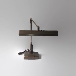May include: A vintage brown metal desk lamp with a long, adjustable arm and a rectangular light fixture. The lamp has a simple, functional design.