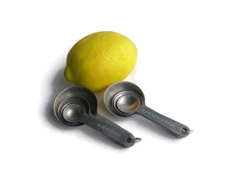 May include: A bright yellow lemon next to a set of four stainless steel measuring spoons. The spoons are labeled with their measurements, including 1/4 teaspoon and 1 teaspoon. The spoons have a matte finish and a small hole at the end of the handle.