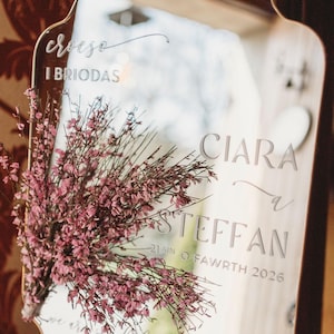 Puede incluir: Espejo decorativo con marco dorado, grabado con nombres y fecha. Muestra los nombres "Ciara & Steffan" y la fecha "21ain o Fawrth 2026". Un ramo de flores rosas adorna el espejo. El texto "Croeso I Briodas" est&aacute; grabado.