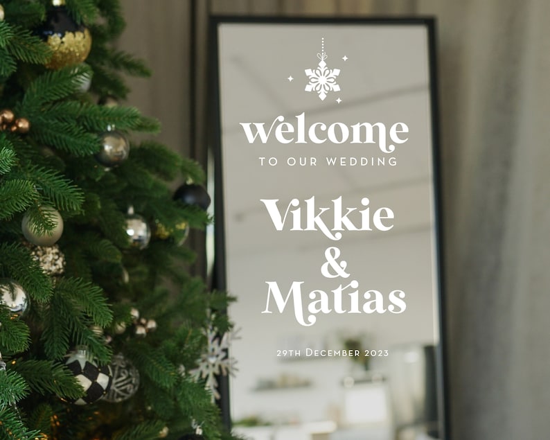 May include: A white sign with a snowflake design and the text "welcome to our wedding Vikkie & Matias 29th December 2023" reflected in a mirror.