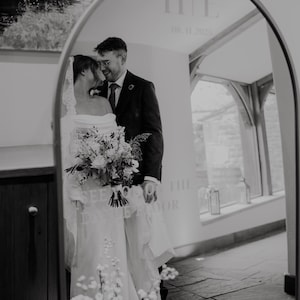 A black and white image of a bride and groom standing in front of a mirror, with the bride holding a bouquet of flowers.