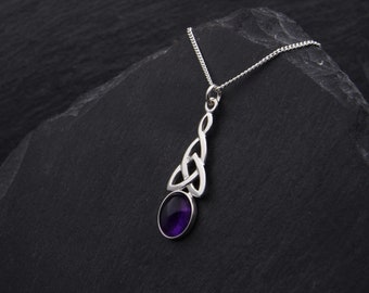 May include: A silver Celtic knot pendant necklace with a purple amethyst gemstone. The necklace is displayed on a black slate background.