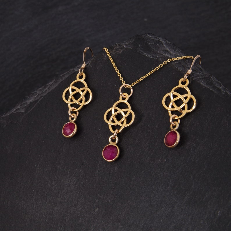 May include: A gold necklace and earrings set with a Celtic knot design and ruby red stones.