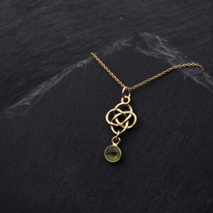 May include: A gold necklace with a Celtic knot pendant and a green gemstone. The necklace is on a black background.