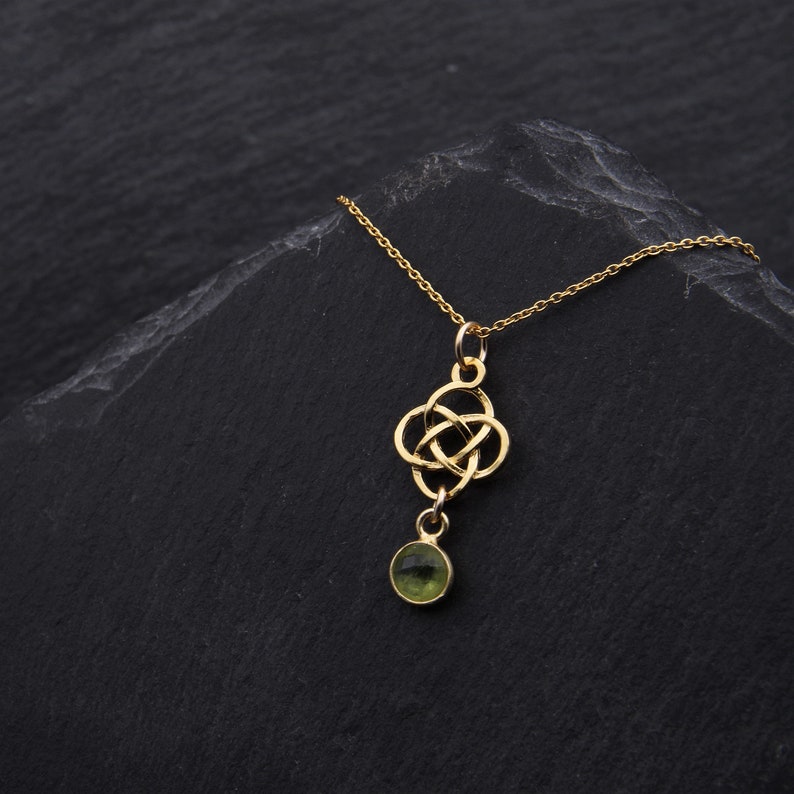 May include: A gold necklace with a Celtic knot pendant and a green gemstone. The necklace is on a black background.