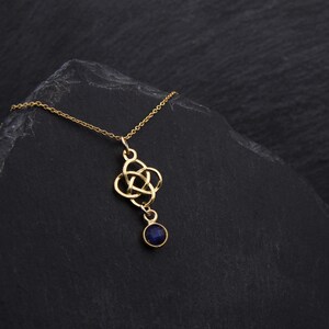 May include: A gold necklace with a Celtic knot pendant and a dark blue gemstone. The necklace is on a black background.
