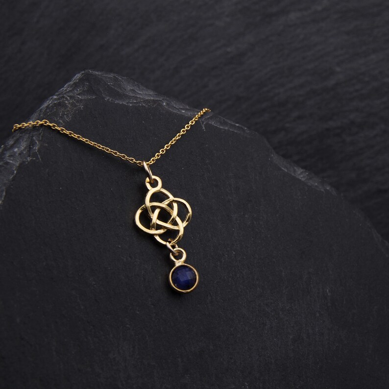 May include: A gold necklace with a Celtic knot pendant and a dark blue gemstone. The necklace is on a black background.