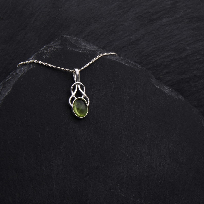 May include: A silver chain necklace with a green gemstone pendant. The pendant is in a Celtic knot design.