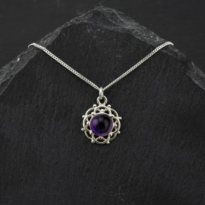 May include: A silver necklace with a purple amethyst gemstone pendant set in a delicate silver filigree design.