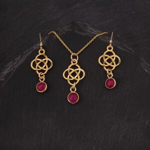 May include: A gold necklace and earrings set with a Celtic knot design and red gemstone accents.