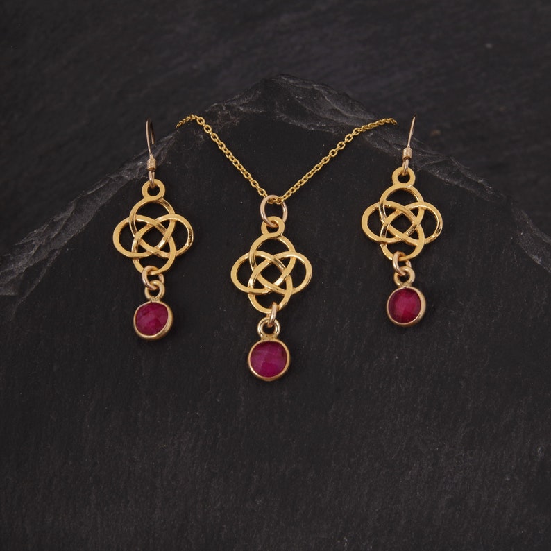 May include: A gold necklace and earrings set with a Celtic knot design and red gemstone accents.