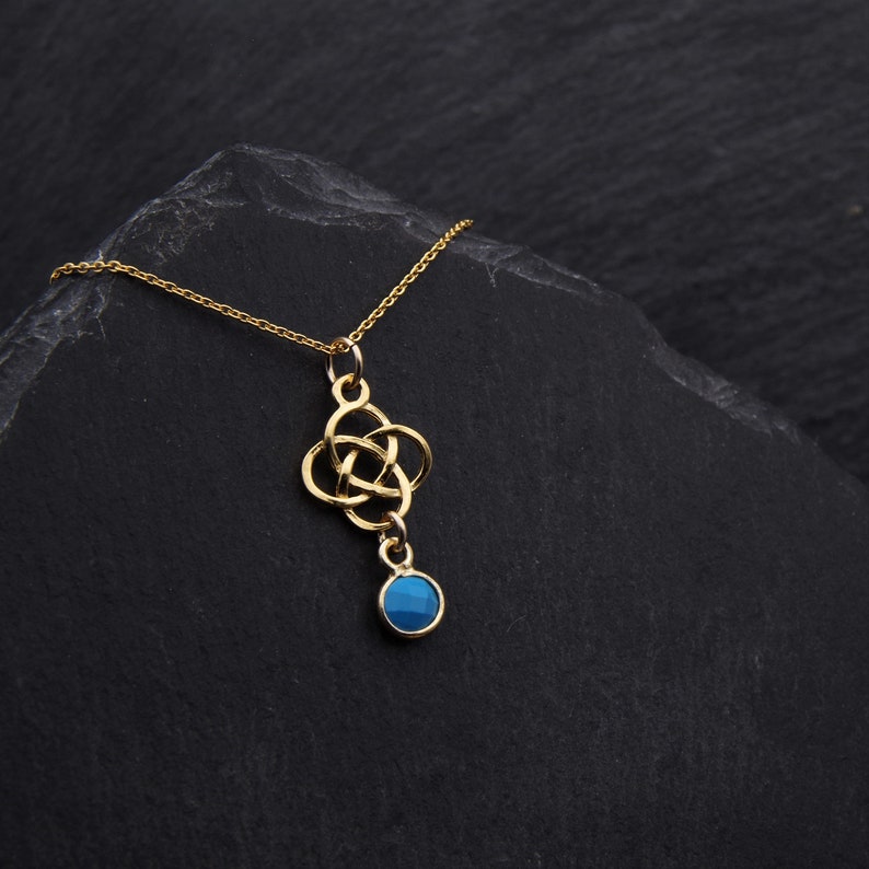 May include: A gold necklace with a Celtic knot pendant and a blue gemstone. The necklace is on a black background.
