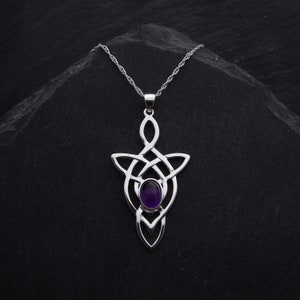 Puede incluir: Un collar de plata con un colgante de nudo celta con una amatista púrpura en el centro.