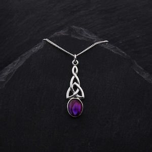 May include: A silver Celtic knot pendant necklace with a purple abalone shell inlay. The necklace is on a black background.