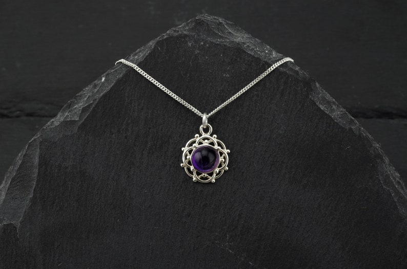 May include: A silver necklace with a purple amethyst gemstone set in a delicate, circular, filigree pendant.