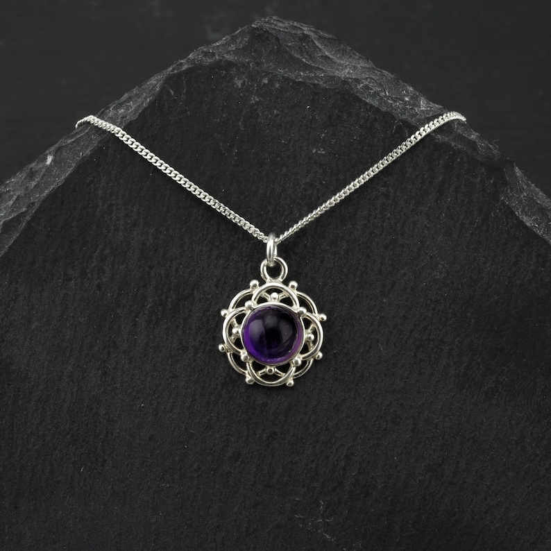May include: A silver necklace with a purple amethyst gemstone pendant set in a delicate silver filigree design.