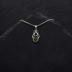 May include: A silver chain necklace with a green gemstone pendant. The pendant is in a Celtic knot design.