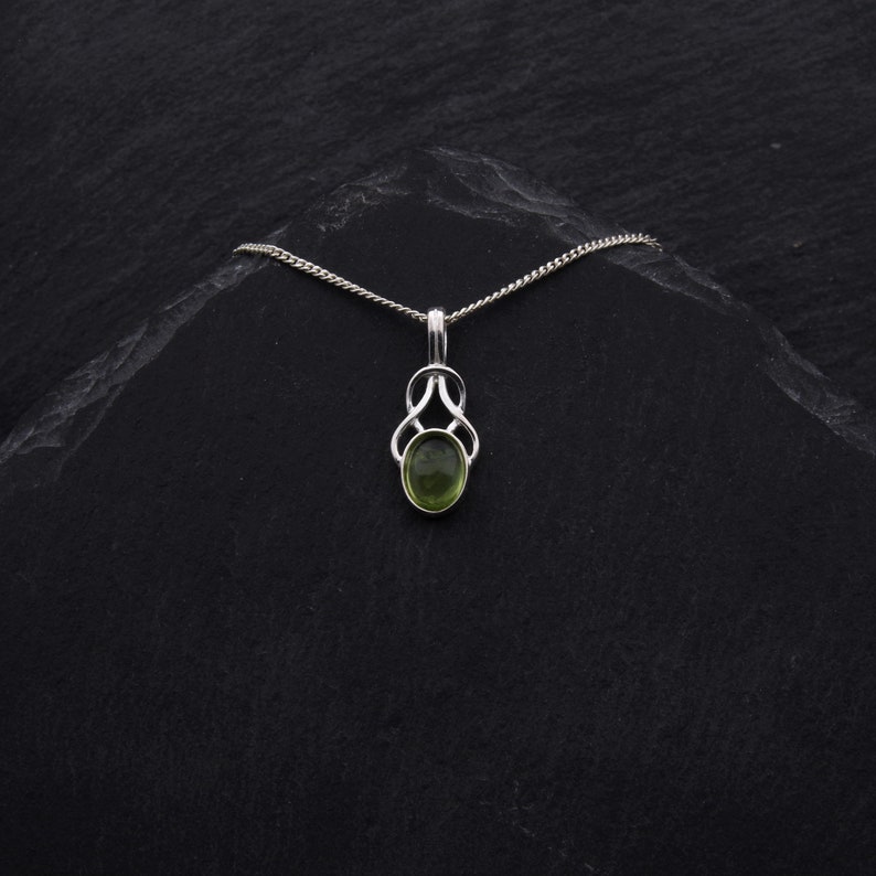 May include: A silver chain necklace with a green gemstone pendant. The pendant is in a Celtic knot design.