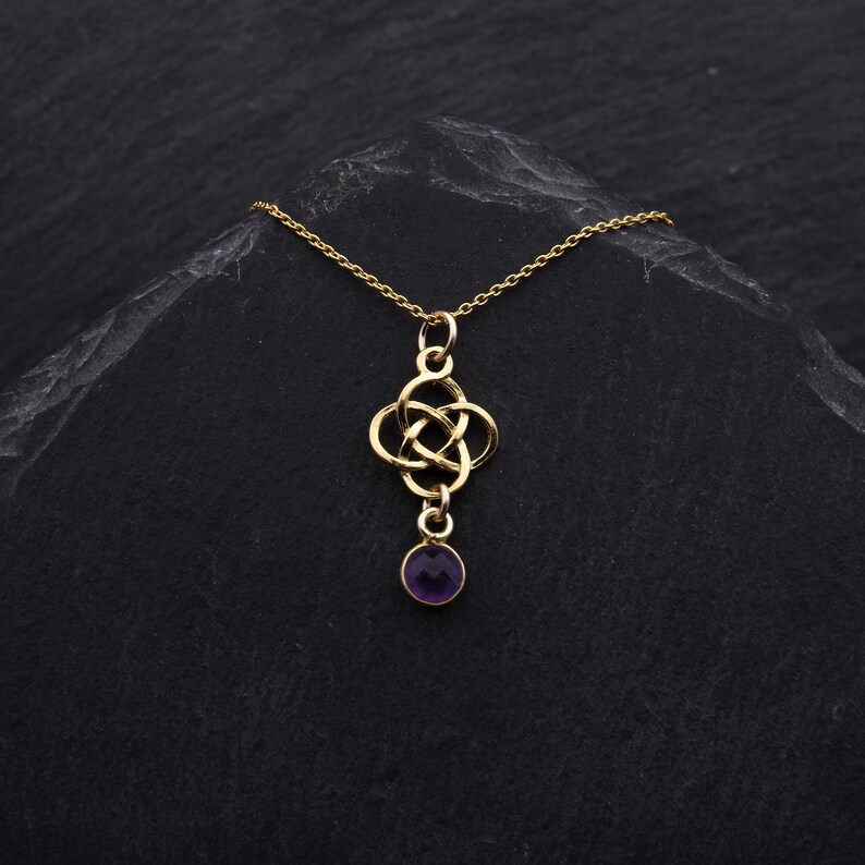May include: A gold necklace with a Celtic knot pendant and a purple gemstone. The necklace is on a black background.